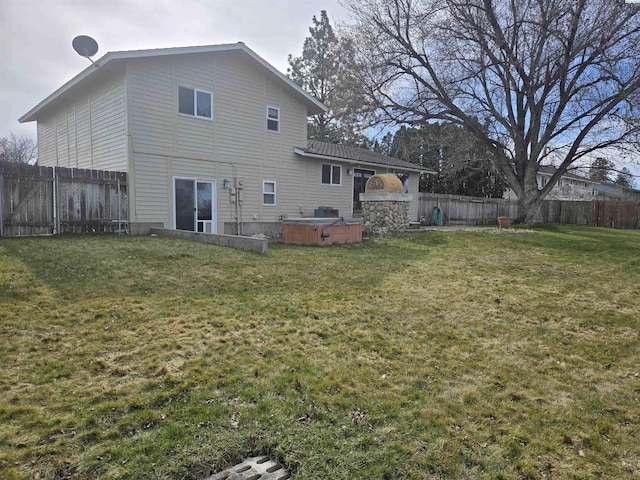 back of property with a yard, a fenced backyard, and a hot tub