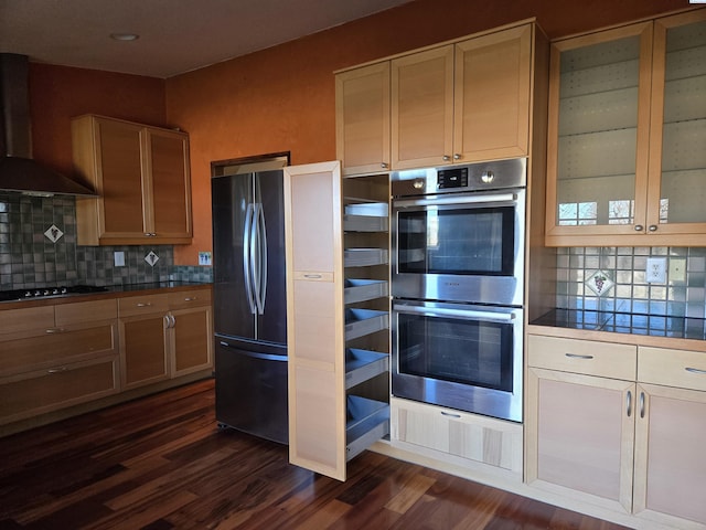 kitchen with wall chimney range hood, appliances with stainless steel finishes, backsplash, and dark wood-style flooring