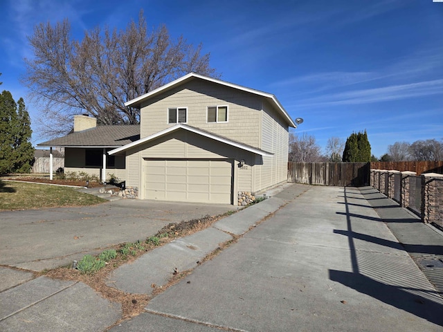 view of home's exterior with a garage, concrete driveway, fence, and a chimney