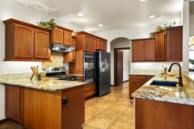 kitchen featuring light stone counters, a sink, appliances with stainless steel finishes, a peninsula, and under cabinet range hood