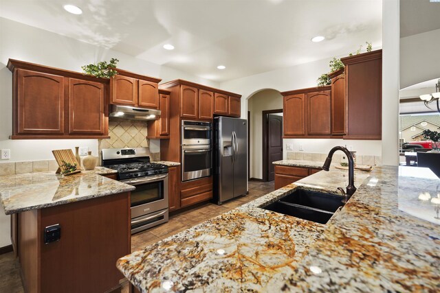 kitchen with a peninsula, stainless steel appliances, arched walkways, under cabinet range hood, and a sink