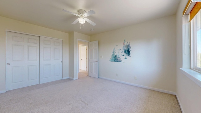 unfurnished bedroom featuring baseboards, ceiling fan, a closet, and light colored carpet