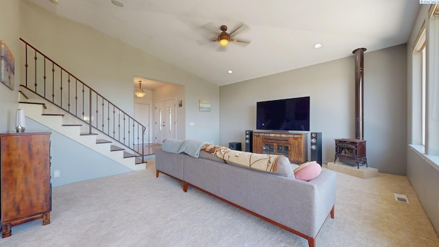 carpeted living room featuring ceiling fan, visible vents, a wood stove, lofted ceiling, and stairs