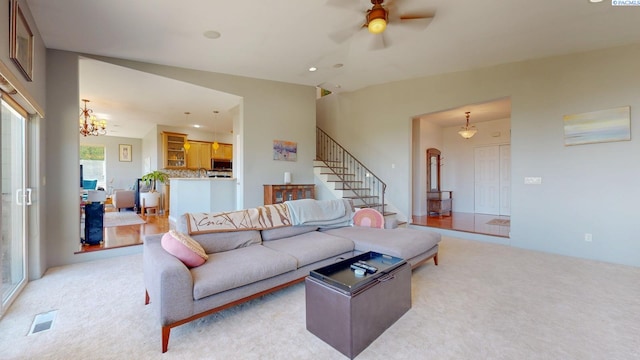 living room with stairway, light carpet, ceiling fan with notable chandelier, and visible vents