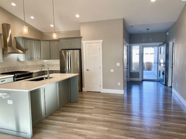kitchen with wall chimney range hood, light countertops, decorative backsplash, appliances with stainless steel finishes, and a sink