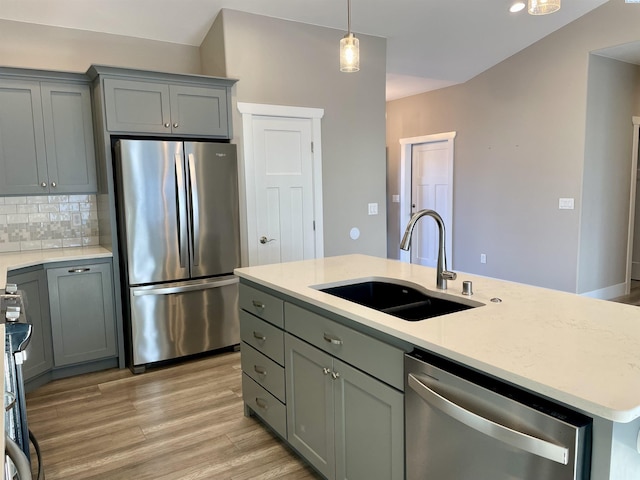 kitchen featuring backsplash, gray cabinetry, light wood-style floors, stainless steel appliances, and a sink