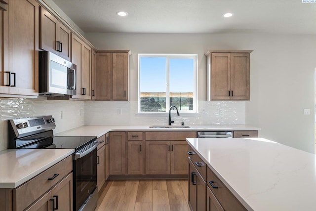 kitchen with sink, light stone counters, light hardwood / wood-style flooring, appliances with stainless steel finishes, and backsplash