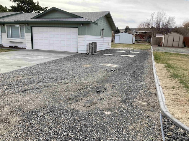 view of side of home featuring driveway, a garage, roof with shingles, an outbuilding, and a storage unit