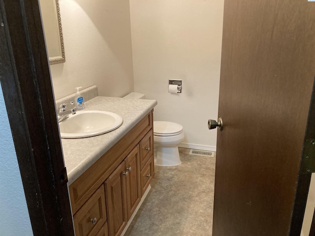 half bathroom with toilet, vanity, visible vents, and baseboards