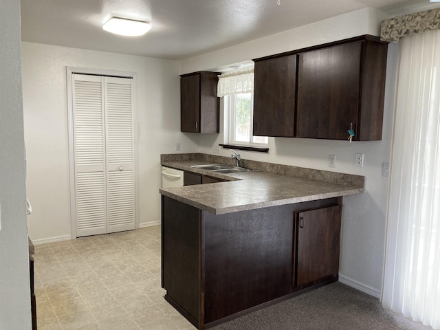 kitchen with dark brown cabinets, a peninsula, a sink, and baseboards