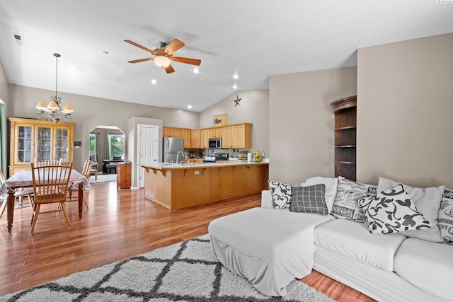 living room with lofted ceiling, ceiling fan with notable chandelier, and light hardwood / wood-style flooring