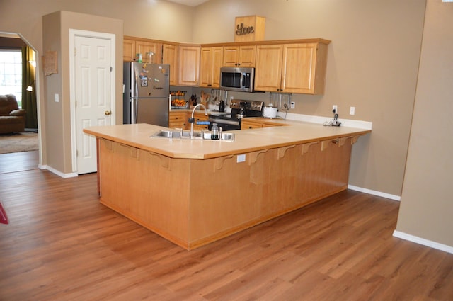 kitchen with sink, light hardwood / wood-style flooring, stainless steel appliances, and kitchen peninsula