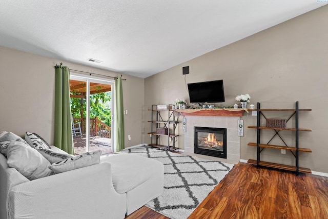 living room with hardwood / wood-style flooring, vaulted ceiling, a tile fireplace, and a textured ceiling