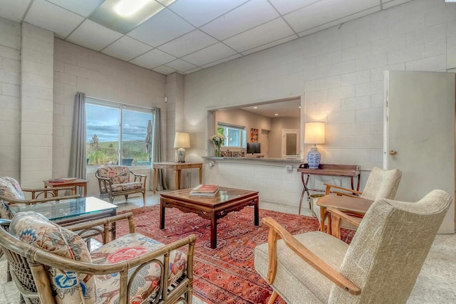 living room with a paneled ceiling and concrete block wall