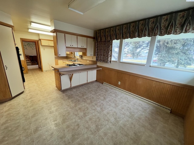 kitchen featuring wainscoting, a peninsula, baseboard heating, light countertops, and light floors