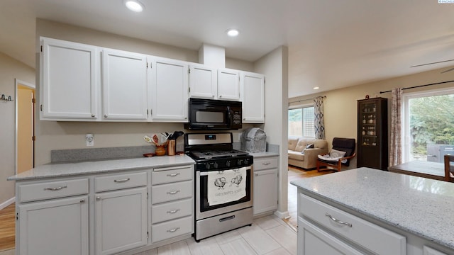 kitchen with a wealth of natural light, white cabinets, black microwave, and stainless steel gas range