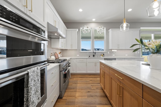 kitchen featuring sink, white cabinetry, hanging light fixtures, stainless steel appliances, and light stone countertops