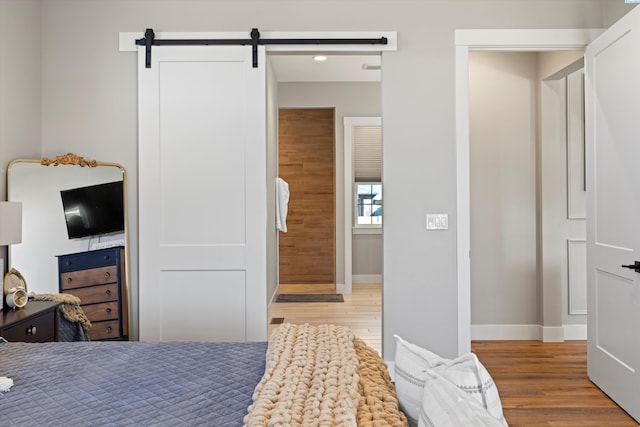 bedroom with a barn door and light wood-type flooring