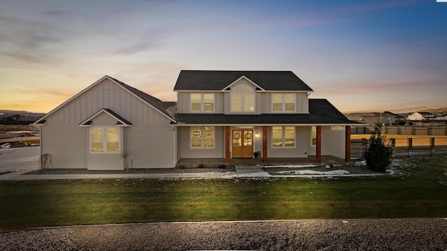 back house at dusk featuring a lawn and covered porch