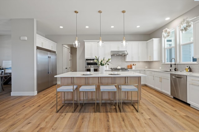 kitchen with sink, a kitchen island, pendant lighting, stainless steel appliances, and white cabinets