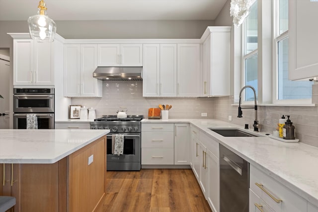 kitchen with extractor fan, appliances with stainless steel finishes, sink, white cabinets, and hanging light fixtures