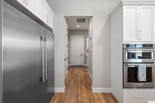 kitchen featuring wood-type flooring, stainless steel appliances, and white cabinets