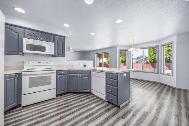 8307 Camano Dr, Pasco, WA 99301 - kitchen featuring white appliances, a peninsula, gray cabinetry, wood finished floors, and a textured ceiling