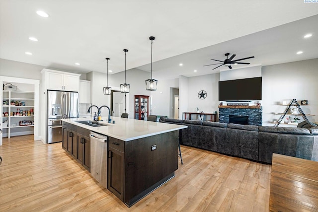 kitchen with sink, a center island with sink, pendant lighting, stainless steel appliances, and white cabinets