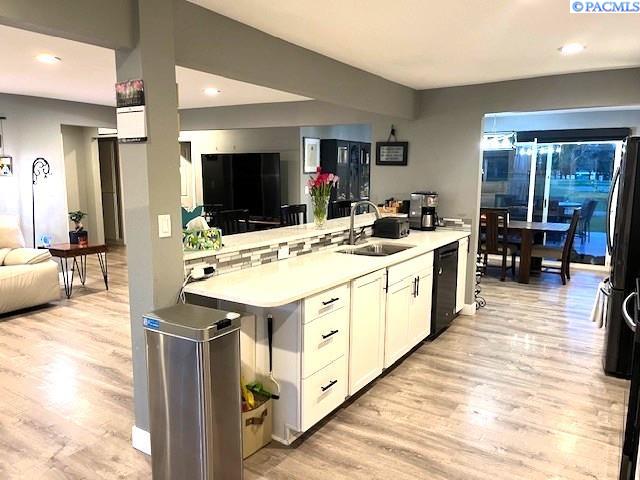 kitchen with a sink, black appliances, light wood finished floors, light countertops, and white cabinets