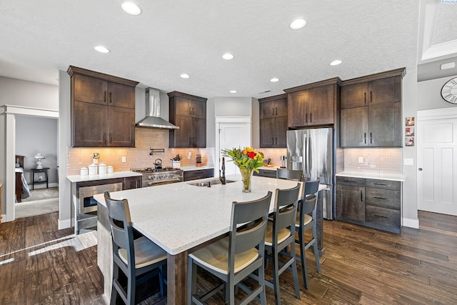 kitchen featuring wall chimney exhaust hood, stainless steel appliances, a sink, dark brown cabinets, and recessed lighting
