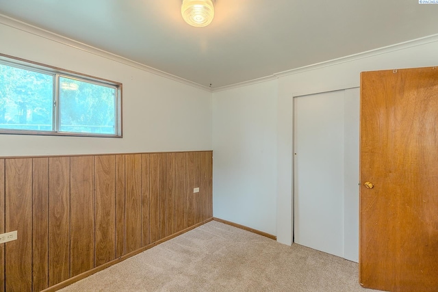 unfurnished bedroom with a closet, ornamental molding, wooden walls, and light carpet