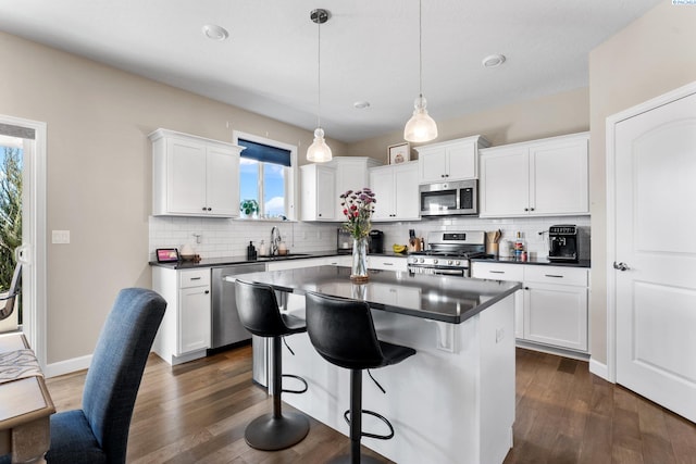 kitchen with dark countertops, a breakfast bar, white cabinets, stainless steel appliances, and a sink