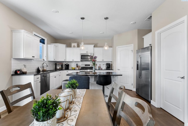 kitchen with dark countertops, backsplash, a kitchen island, appliances with stainless steel finishes, and a sink