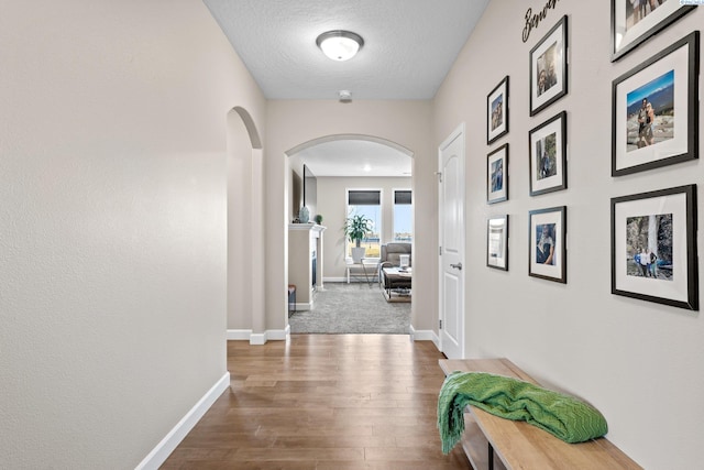 hall featuring arched walkways, a textured ceiling, dark wood-type flooring, and baseboards