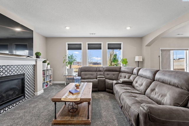 living area featuring visible vents, baseboards, a textured ceiling, a tiled fireplace, and dark colored carpet