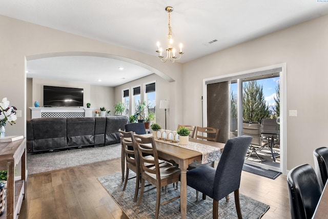 dining room with hardwood / wood-style flooring, a notable chandelier, arched walkways, and visible vents