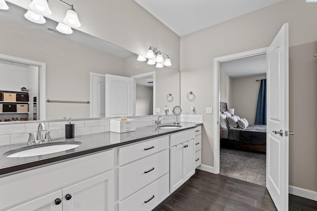 ensuite bathroom with baseboards, double vanity, ensuite bathroom, wood finished floors, and a sink