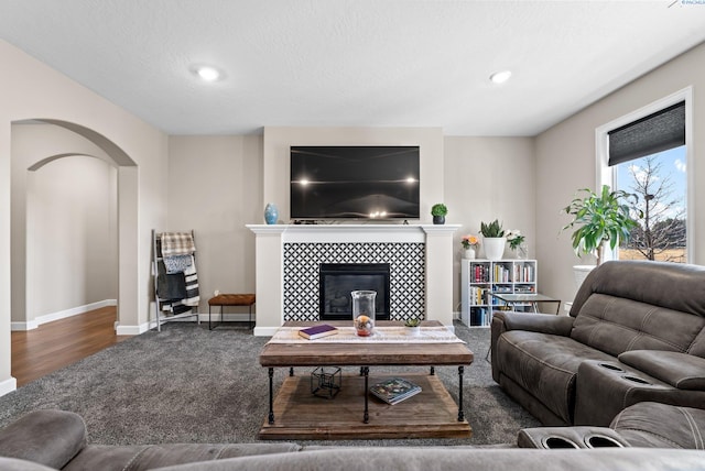 living area with baseboards, carpet flooring, recessed lighting, a tile fireplace, and arched walkways