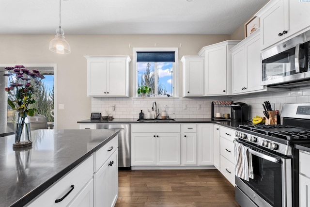 kitchen with dark countertops, a sink, white cabinets, stainless steel appliances, and dark wood-style flooring