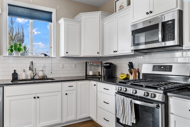 kitchen with dark countertops, backsplash, white cabinets, stainless steel appliances, and a sink