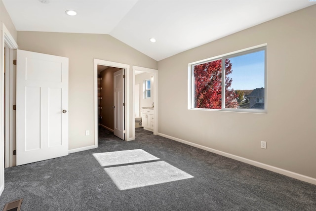 unfurnished bedroom with dark colored carpet, vaulted ceiling, and ensuite bath