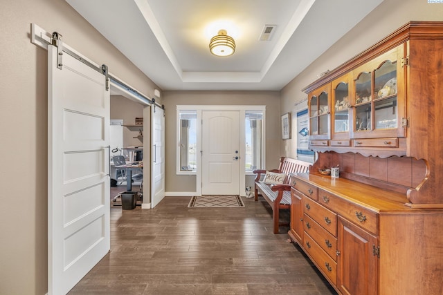 foyer with a raised ceiling, a barn door, and dark wood-type flooring