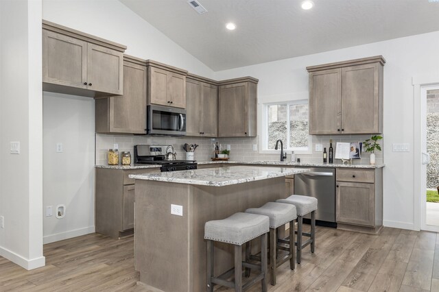 kitchen featuring appliances with stainless steel finishes, a center island, light stone counters, vaulted ceiling, and light wood-type flooring