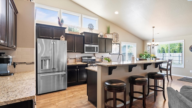 kitchen featuring light wood finished floors, stainless steel appliances, tasteful backsplash, an inviting chandelier, and a kitchen bar