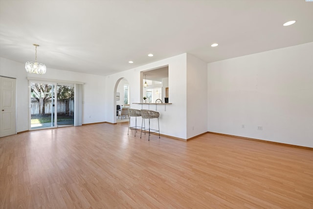 unfurnished living room featuring arched walkways, recessed lighting, an inviting chandelier, light wood-style floors, and baseboards