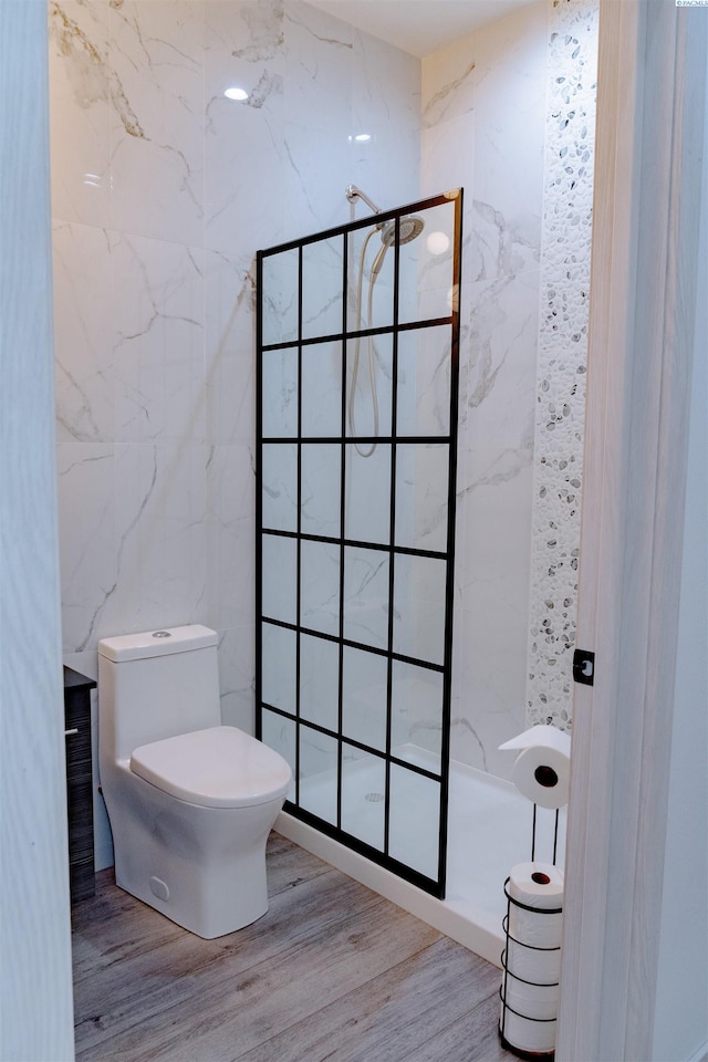 bathroom with toilet, hardwood / wood-style floors, tile walls, and a shower