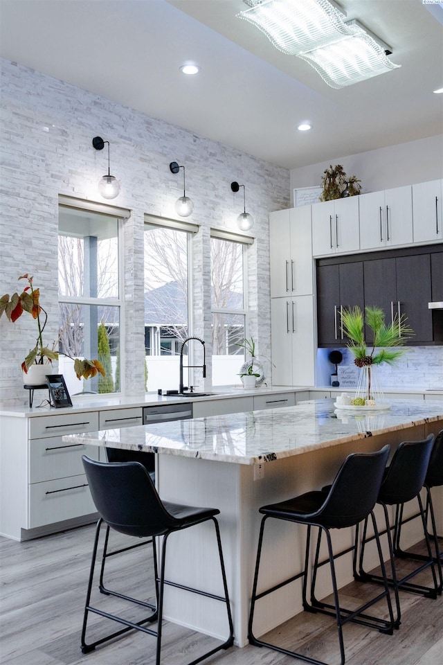 kitchen featuring pendant lighting, sink, a kitchen breakfast bar, light stone counters, and white cabinets