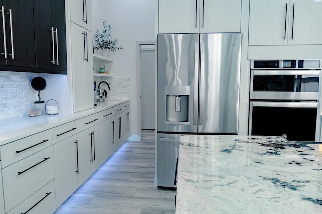 kitchen with light stone counters, decorative backsplash, light hardwood / wood-style flooring, and stainless steel appliances