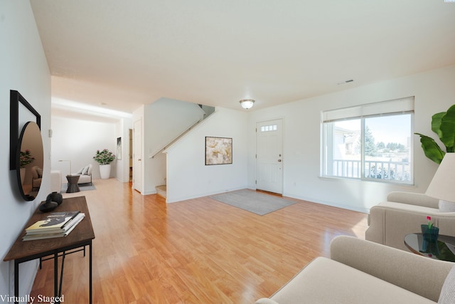 living room featuring stairs, light wood-style floors, visible vents, and baseboards