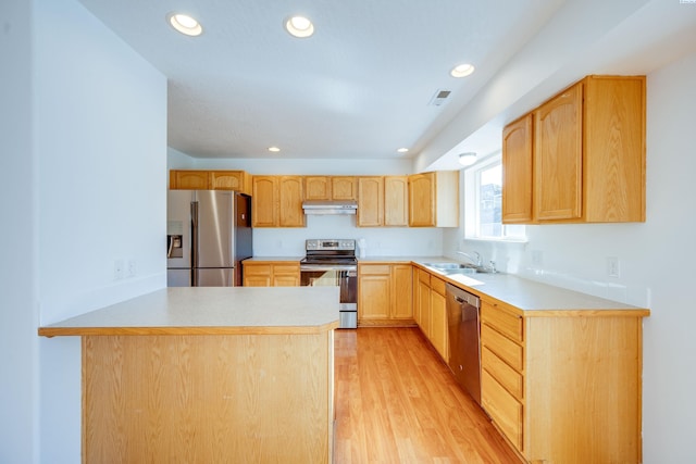 kitchen with light wood finished floors, light brown cabinets, a sink, stainless steel appliances, and light countertops